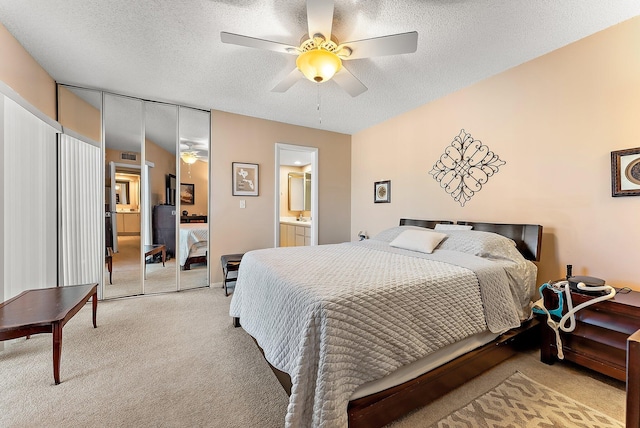 carpeted bedroom featuring ceiling fan, a closet, a textured ceiling, and ensuite bath