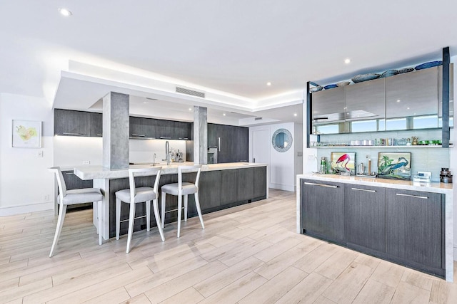 kitchen with a kitchen breakfast bar, dark brown cabinetry, an island with sink, and light hardwood / wood-style flooring