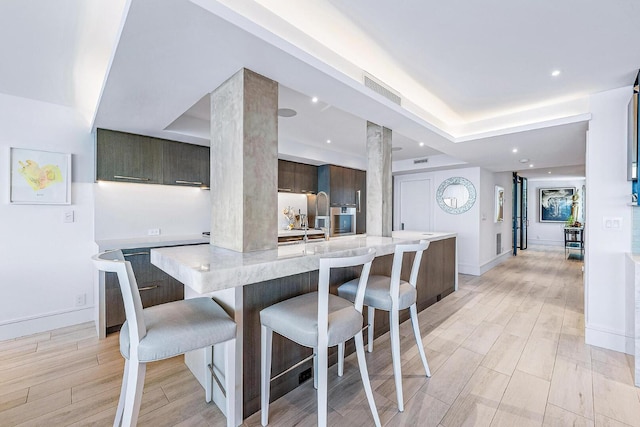 kitchen with a breakfast bar area, ornate columns, light hardwood / wood-style flooring, and a spacious island