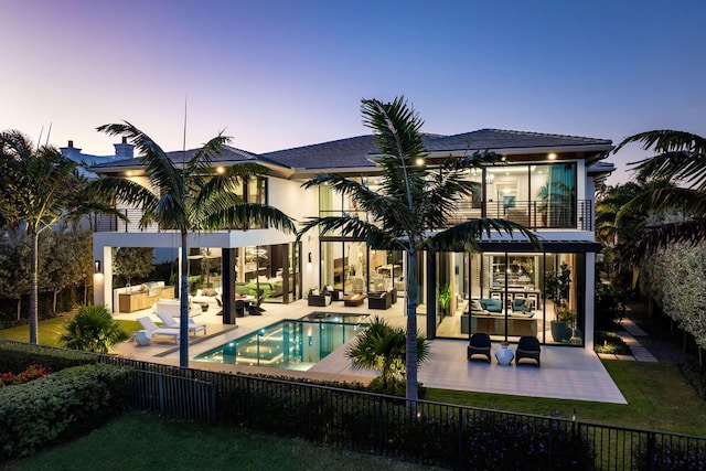 back house at dusk with an outdoor living space, a fenced in pool, an outdoor kitchen, a balcony, and a patio area