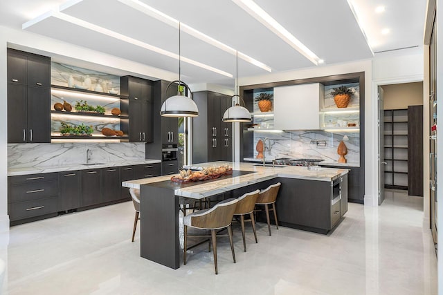 kitchen with light stone countertops, a large island, hanging light fixtures, a kitchen breakfast bar, and decorative backsplash