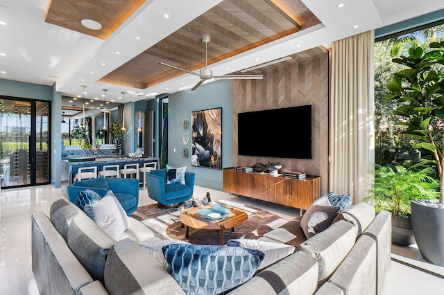 living room featuring a wealth of natural light, expansive windows, a raised ceiling, and ceiling fan