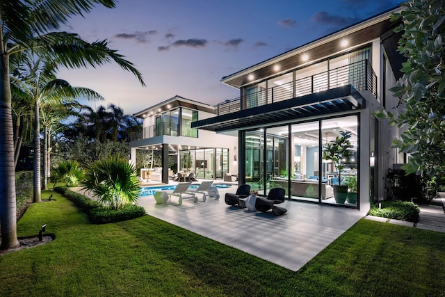 back house at dusk featuring a yard, a patio, and a balcony