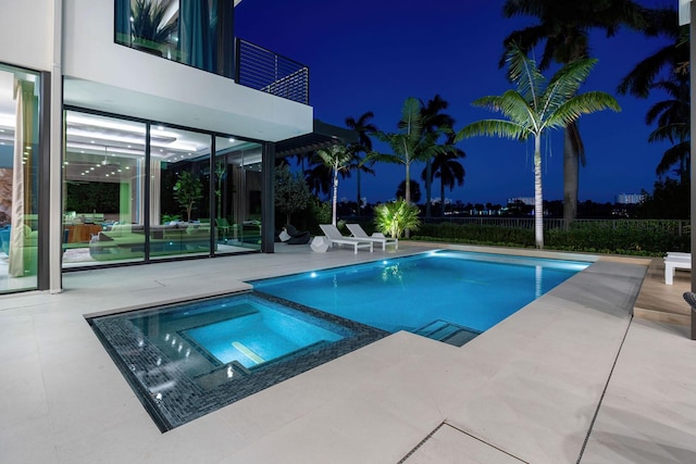 pool at night featuring an in ground hot tub and a patio