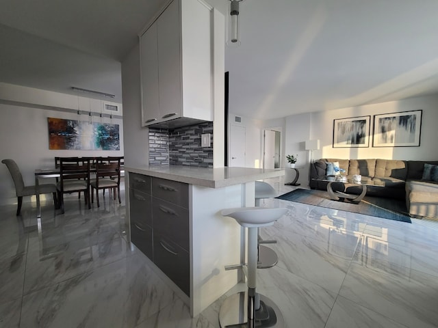 kitchen featuring tasteful backsplash, a breakfast bar, light countertops, marble finish floor, and modern cabinets