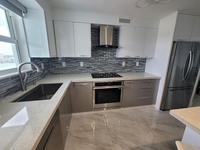 kitchen with sink, light stone counters, appliances with stainless steel finishes, decorative backsplash, and wall chimney range hood