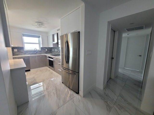 kitchen with wall chimney exhaust hood, sink, white cabinetry, appliances with stainless steel finishes, and decorative backsplash