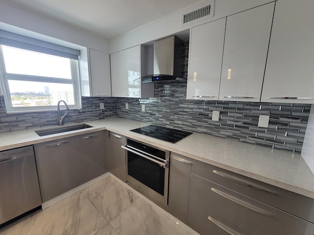 kitchen featuring stainless steel appliances, light stone countertops, sink, backsplash, and wall chimney range hood