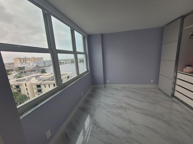 unfurnished room with baseboards, marble finish floor, and a water view