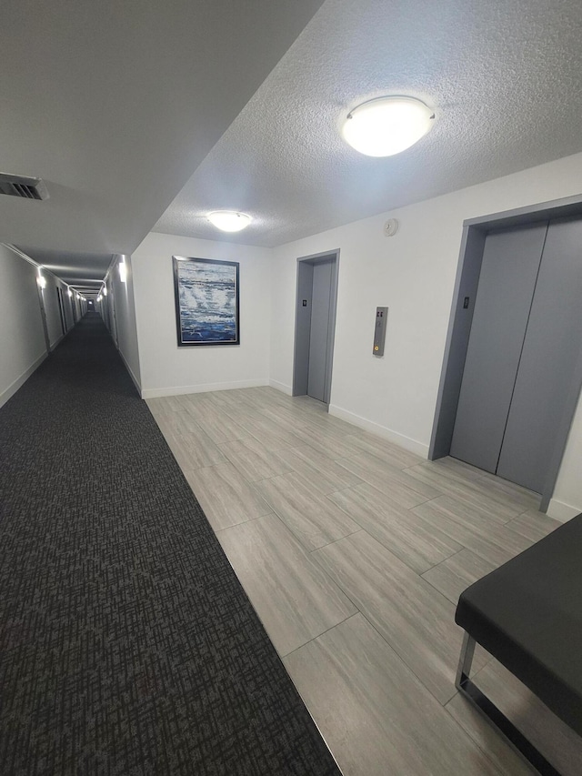 corridor featuring elevator and a textured ceiling