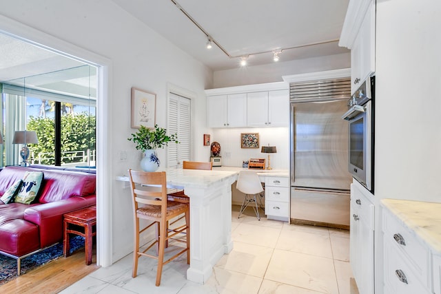 kitchen with light stone countertops, stainless steel appliances, a kitchen breakfast bar, white cabinets, and built in desk