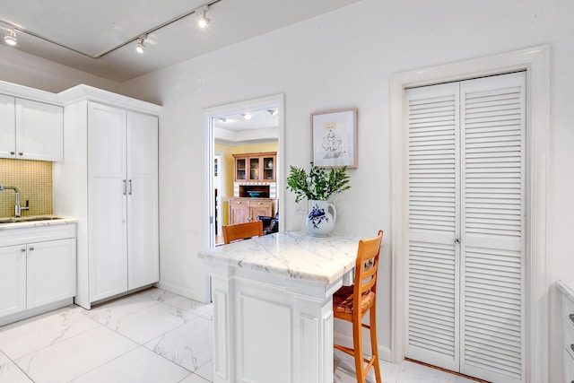 kitchen with white cabinets, track lighting, light stone counters, and sink