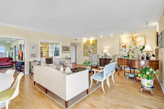 living room with crown molding, light hardwood / wood-style flooring, rail lighting, and beverage cooler