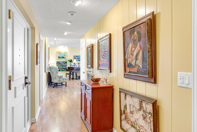 corridor with wood walls, light hardwood / wood-style floors, and a textured ceiling