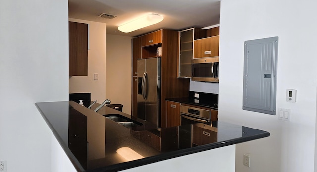 kitchen featuring sink, electric panel, kitchen peninsula, dark stone counters, and appliances with stainless steel finishes