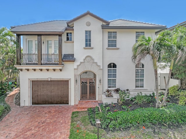 mediterranean / spanish home featuring an attached garage, a tiled roof, decorative driveway, and stucco siding