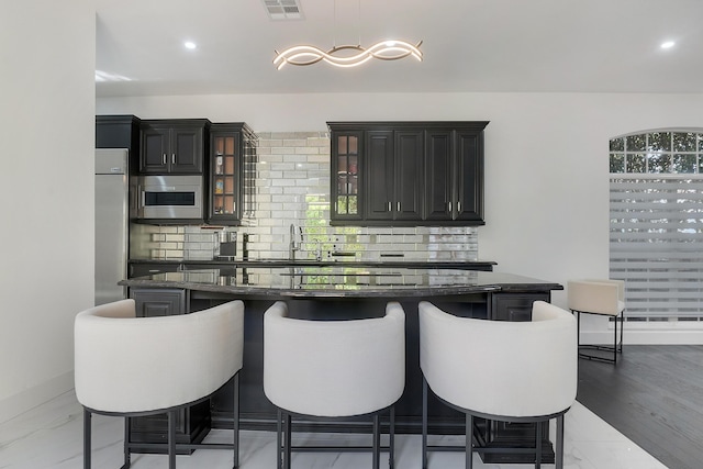 bar with hanging light fixtures, tasteful backsplash, built in microwave, and dark stone counters