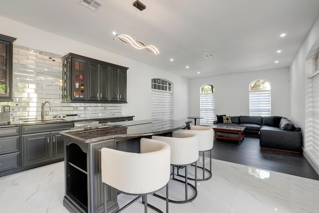 kitchen featuring sink, hanging light fixtures, backsplash, dark stone counters, and a kitchen island