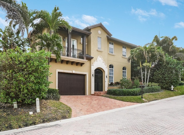 mediterranean / spanish home featuring a garage, decorative driveway, a balcony, and stucco siding