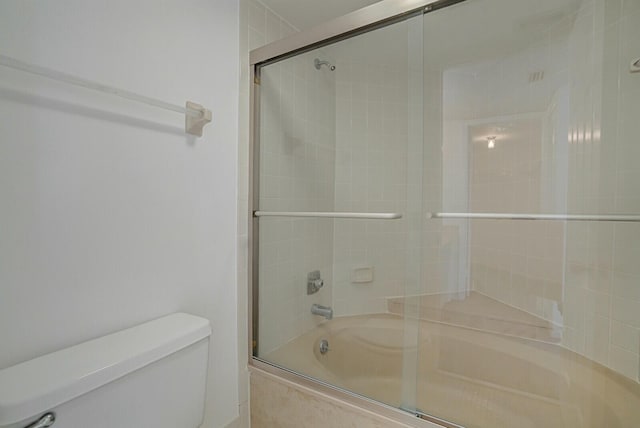 bathroom featuring toilet and combined bath / shower with glass door