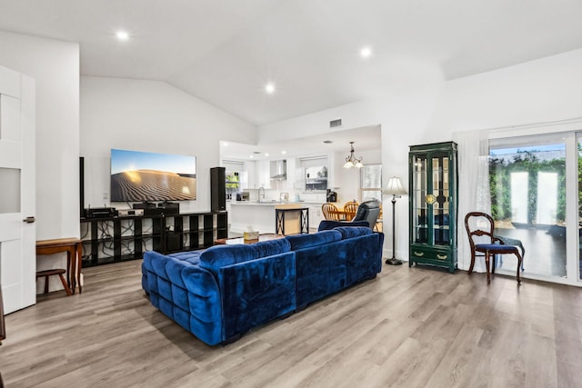 living room featuring vaulted ceiling, an inviting chandelier, sink, and light hardwood / wood-style flooring