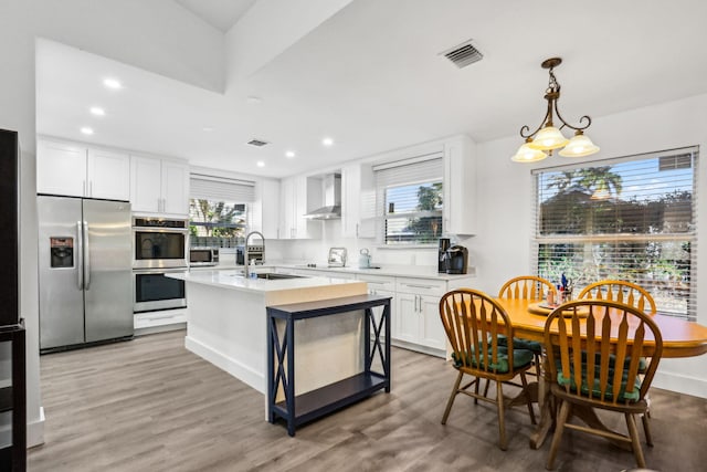 kitchen featuring white cabinets, sink, light hardwood / wood-style flooring, wall chimney exhaust hood, and appliances with stainless steel finishes