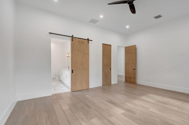 unfurnished bedroom with connected bathroom, a barn door, ceiling fan, and light wood-type flooring