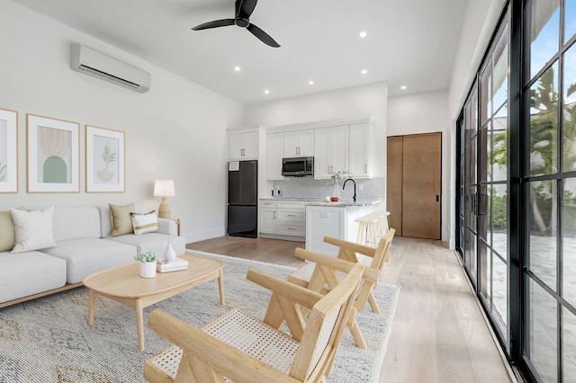 living room with a wall mounted air conditioner, ceiling fan, light wood-type flooring, and sink