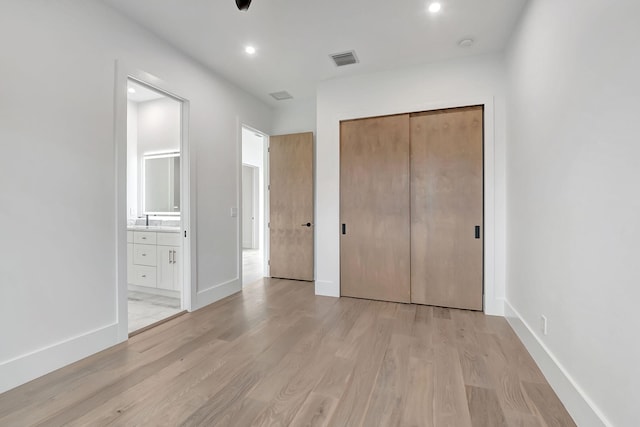 unfurnished bedroom featuring a closet, ensuite bathroom, and light hardwood / wood-style flooring