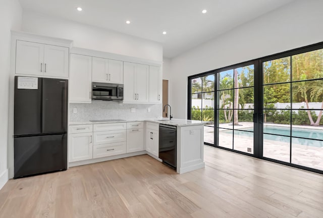 kitchen featuring kitchen peninsula, sink, black appliances, light hardwood / wood-style floors, and white cabinetry