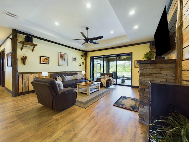 living room with a raised ceiling, crown molding, ceiling fan, light wood-type flooring, and a fireplace