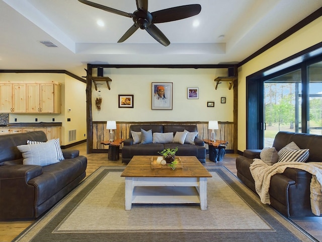 living room featuring a tray ceiling, ceiling fan, ornamental molding, and hardwood / wood-style flooring