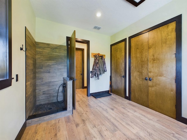 bathroom with wood-type flooring, a textured ceiling, and a tile shower