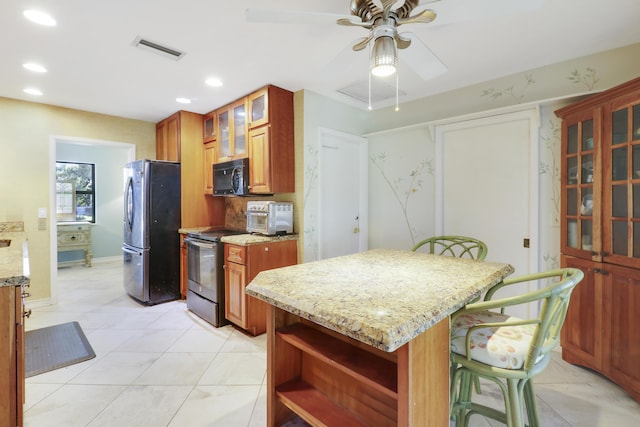 kitchen featuring light stone countertops, a kitchen breakfast bar, stainless steel appliances, ceiling fan, and a kitchen island