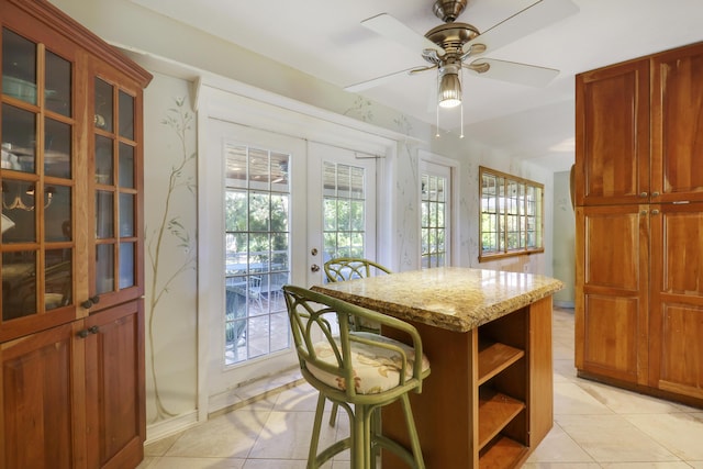 kitchen with ceiling fan, french doors, a center island, light stone counters, and light tile patterned floors