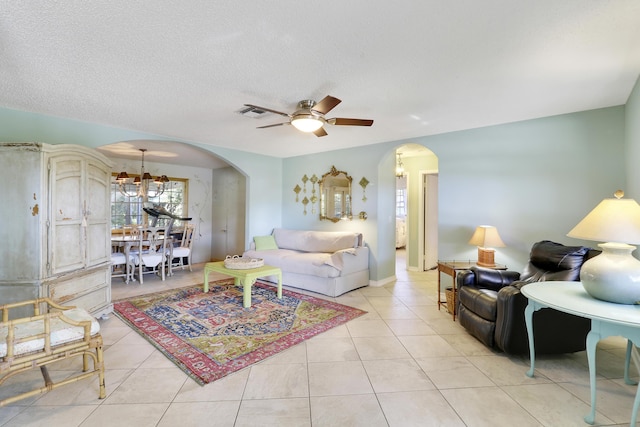 living room featuring a textured ceiling, light tile patterned flooring, and ceiling fan with notable chandelier