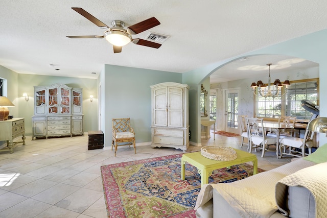 living room with ceiling fan with notable chandelier, light tile patterned floors, and a textured ceiling