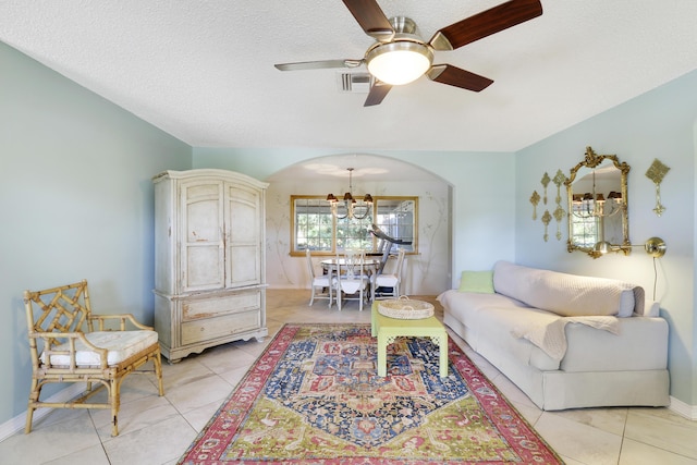 living room featuring a textured ceiling, light tile patterned flooring, and ceiling fan with notable chandelier