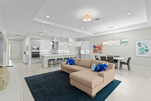 living room featuring a tray ceiling and light tile patterned flooring