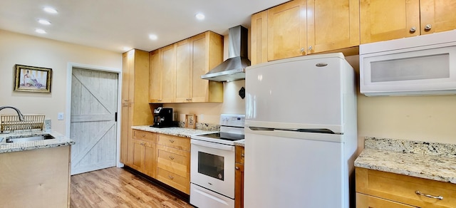 kitchen with light stone countertops, light wood-type flooring, wall chimney exhaust hood, white appliances, and sink