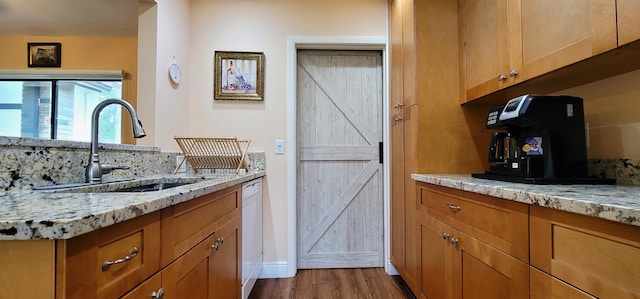 kitchen featuring hardwood / wood-style flooring, dishwasher, light stone countertops, and sink