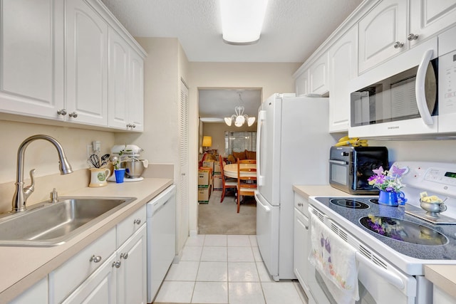 kitchen featuring white appliances, sink, light tile patterned floors, a notable chandelier, and white cabinets