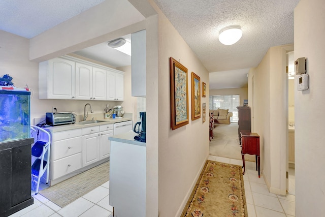 kitchen with dishwasher, light tile patterned floors, white cabinetry, and sink