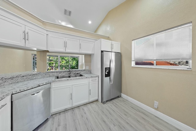 kitchen with light stone counters, stainless steel appliances, vaulted ceiling, sink, and white cabinets