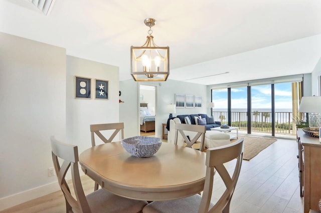 dining space featuring a chandelier, light wood-type flooring, a water view, and floor to ceiling windows