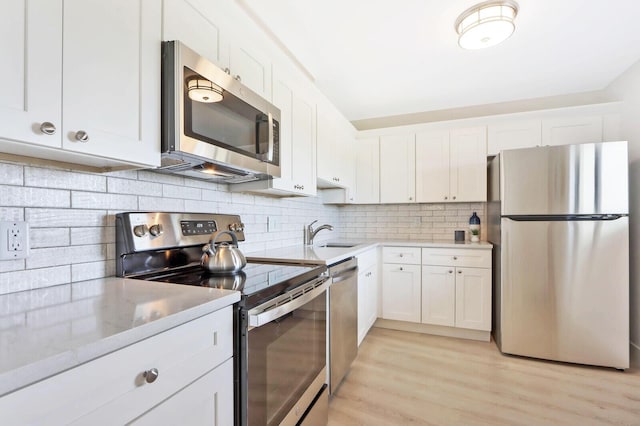 kitchen featuring decorative backsplash, appliances with stainless steel finishes, sink, light hardwood / wood-style flooring, and white cabinets