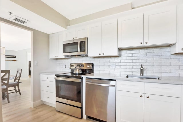 kitchen with decorative backsplash, appliances with stainless steel finishes, sink, light hardwood / wood-style flooring, and white cabinetry