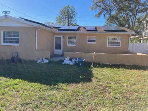 rear view of house with solar panels and a yard