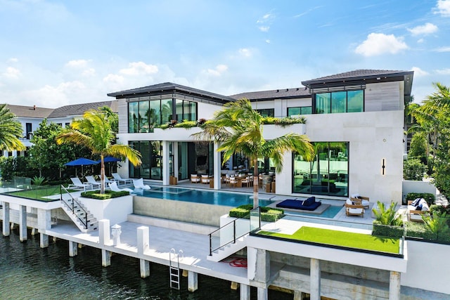 rear view of house featuring a water view, a balcony, a pool with hot tub, and a patio area