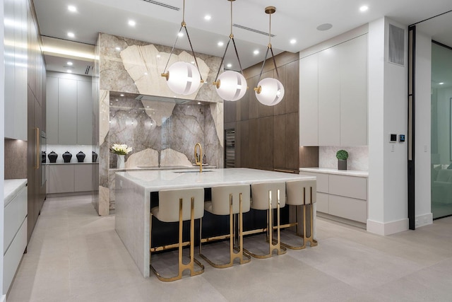 kitchen with white cabinets, decorative light fixtures, backsplash, and a large island with sink